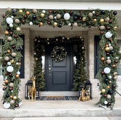 a front porch decorated for christmas with ornaments and greenery on the door, along with two gold deer statues