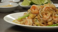 a white plate topped with rice and shrimp next to bowls of lime wedged lettuce