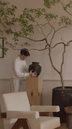 a man standing next to a tree in a living room filled with furniture and potted plants