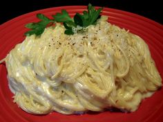 a red plate topped with pasta covered in sauce and garnished with parsley