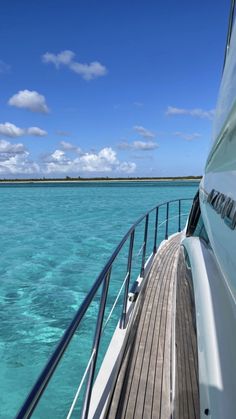 the deck of a boat with clear blue water and clouds in the sky behind it