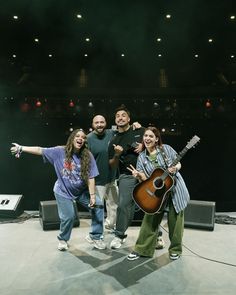 four people posing for a photo while holding their arms in the air and one person with an acoustic guitar