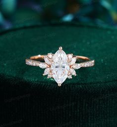 an engagement ring with a pear shaped diamond surrounded by small round diamonds on a green velvet cushion