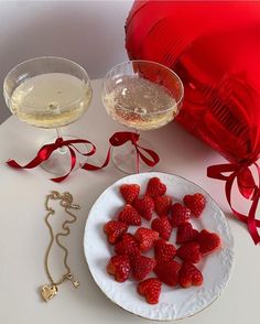 strawberries on a plate next to two glasses of wine and a heart - shaped balloon