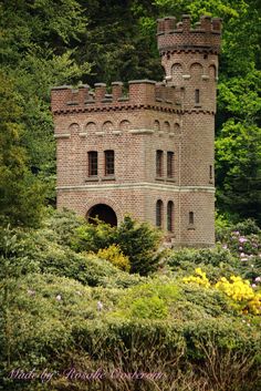 an old brick castle surrounded by trees and flowers in the woods on a sunny day