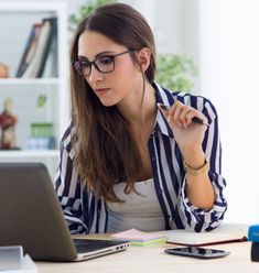 a woman sitting at a desk with a laptop computer in front of her and looking at the screen