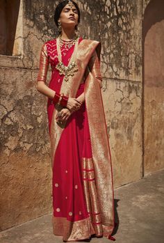 a woman wearing a red and gold sari standing in front of a stone wall