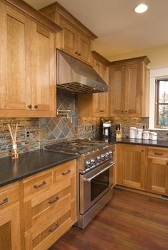 a kitchen with wooden cabinets and black counter tops, stainless steel appliances and wood flooring