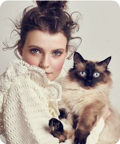 a woman holding a cat in her arms and posing for the camera with blue eyes