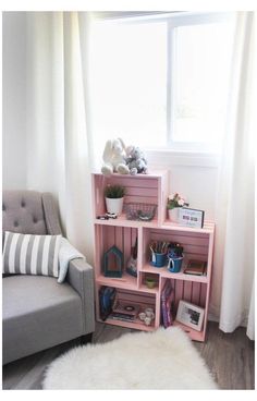 a pink book shelf sitting in front of a window next to a gray chair and white rug