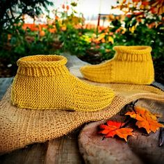 two pairs of yellow knitted shoes sitting on top of a wooden table next to autumn leaves