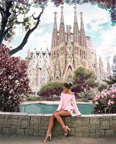 a woman is sitting on a stone wall in front of a building with spires