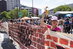 a woman holding up a sign on top of a brick wall in front of a crowd