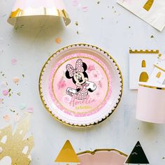 a pink and gold mickey mouse party plate with confetti around it on a table