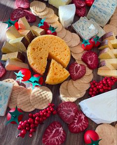 a variety of cheeses and crackers on a wooden table with red berries around them