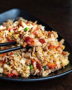 a black plate topped with fried rice and veggies next to chopsticks