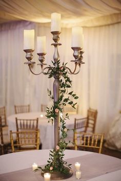 a tall candelabra with candles and greenery on it is surrounded by chairs