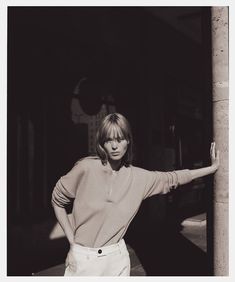 a black and white photo of a woman leaning against a pillar with her arms outstretched