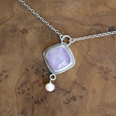 New! Purple Chalcedony Dyna Necklace. Gorgeous and unique Soft, Cool Violet Purple Chalcedony Cushion Square Cabochon is set tipped like a diamond in.925 Sterling Silver - paired with a lustrous, freshwater pearl dangle. All .925 Sterling Silver - includes .925 Sterling Silver chain. We've tipped the square like a diamond for dynamism, and to feature the stone in this new LBJ original. Dyna Necklace in Purple Chalcedony. With a minimal .925 Sterling Silver setting - this Purple Chalcedony Quartz Unique Cabochon Necklaces For Wedding, Sterling Silver Dangle Jewelry With Large Pendant, Sterling Silver Cabochon Jewelry For Anniversary, Sterling Silver Dangle Necklace, Sterling Silver Cabochon Necklace For Anniversary, Artisan Sterling Silver Necklace For Wedding, Artisan Sterling Silver Wedding Necklaces, Artisan Sterling Silver Necklaces For Anniversary, Fine Jewelry Pendant Necklace With Cabochon