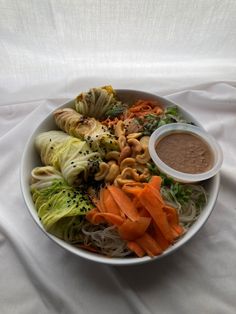 a white bowl filled with pasta and veggies next to dipping sauce on the side