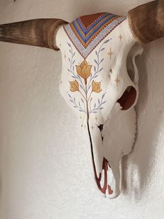 a cow's skull mounted on the wall with decorative paint and wood horns hanging from it