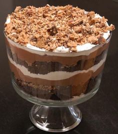 a layered dessert in a glass dish on a black counter top with chocolate and marshmallows