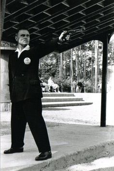 a black and white photo of a man in a suit pointing at something on the ground