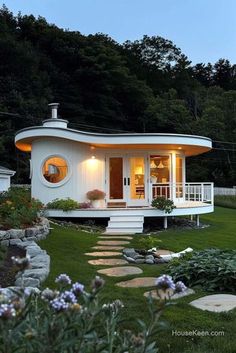 a small white house sitting in the middle of a lush green field with flowers around it