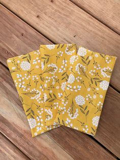 three yellow napkins with white flowers on them sitting on a wooden table next to each other