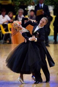 two people dressed in black dancing on a dance floor