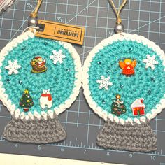 two crocheted christmas ornaments hanging on a piece of paper next to a ruler