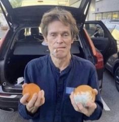 a man holding two donuts in front of his car