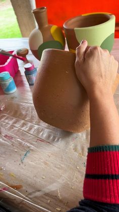 a person is holding a clay pot over a table with other pottery items on it