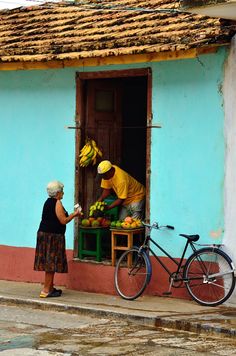 two people are standing in front of a blue building with a bicycle parked next to it