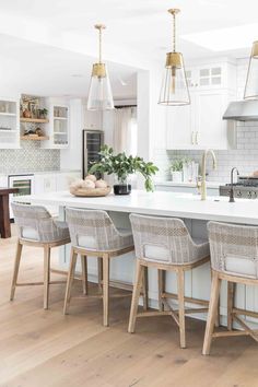 a kitchen with white cabinets and wooden flooring is pictured in this image, there are four chairs at the center of the island