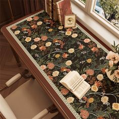 a table with flowers and books on it in front of a window, next to an open book