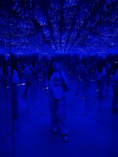 a woman standing in front of a mirror with blue lights hanging from it's ceiling