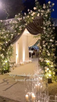 an outdoor ceremony with candles and flowers on the aisle, surrounded by greenery at night