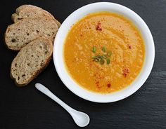 a bowl of soup next to two pieces of bread on a black surface with a spoon