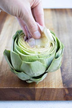 a person is peeling an artichoke on a cutting board