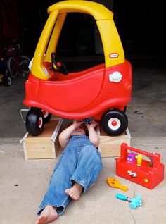 a young child laying on the ground next to a toy car and toolbox set