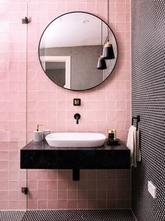 a bathroom with pink tiles and black counter tops, along with a round mirror above the sink