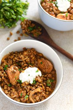 two bowls filled with lentils and meat on top of a table next to parsley