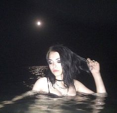 a woman floating in the water at night with her hair blowing back and eyes closed