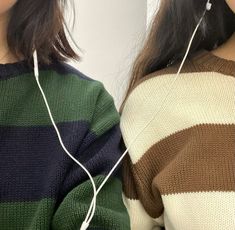 two women wearing ear buds and sweaters, one is looking at the other side