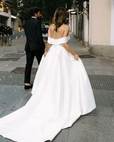 a bride and groom walking down the street in their wedding gowns, looking at each other