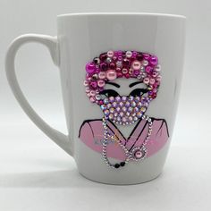 a white coffee cup with a pink and purple beaded woman's face on it