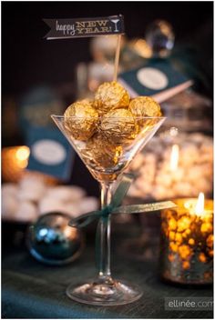 a martini glass filled with gold candies on top of a table next to candles