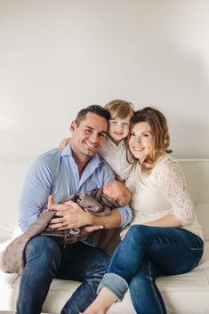 a man, woman and child are sitting on a white couch with their arms around each other