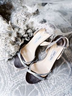 two pairs of shoes sitting on top of a bed next to a bouquet and veil